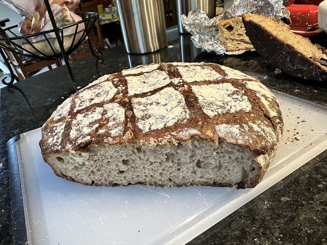 A large round einkorn miche, cut in half to show a dense, even crumb, with a dark crust scored in a diamond pattern and dusted with flour.