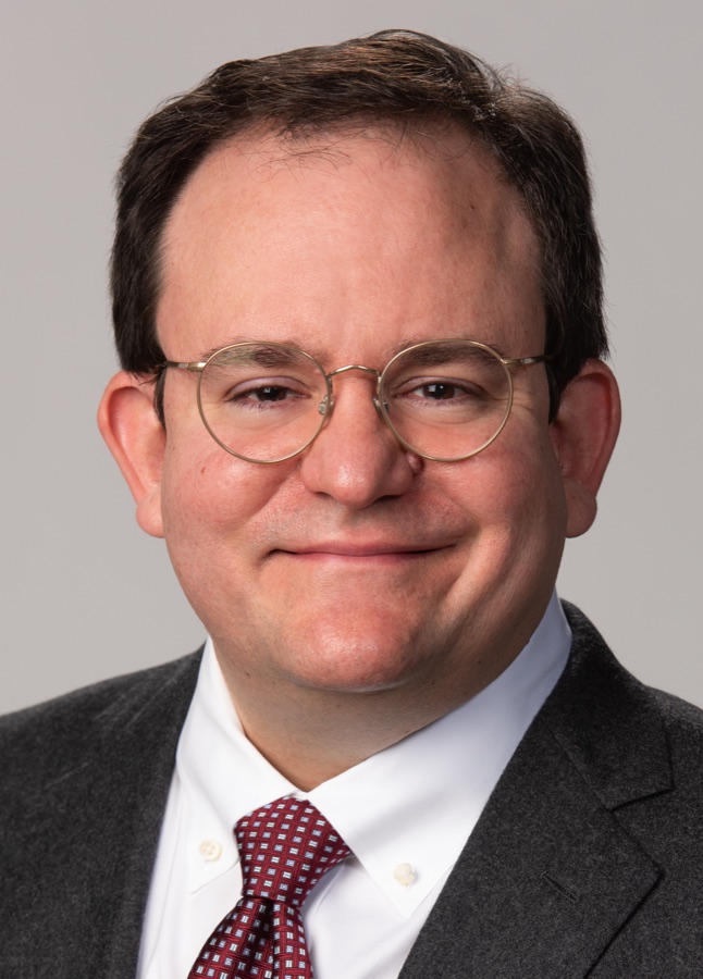 Head-and-shoulders photograph of David Filippi in round wire-rimmed glasses, a dark suit, and a red patterned tie.